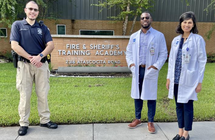 A police officer and two doctors stand outside a police station.