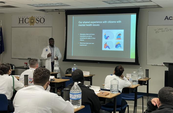 A doctor stands in front of an audience of police officers while giving a presentation.