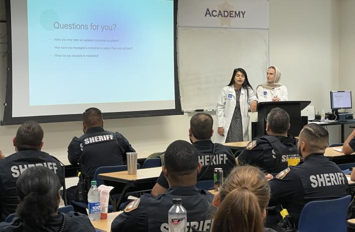 A doctor stands in front of an audience of police officers while giving a presentation.