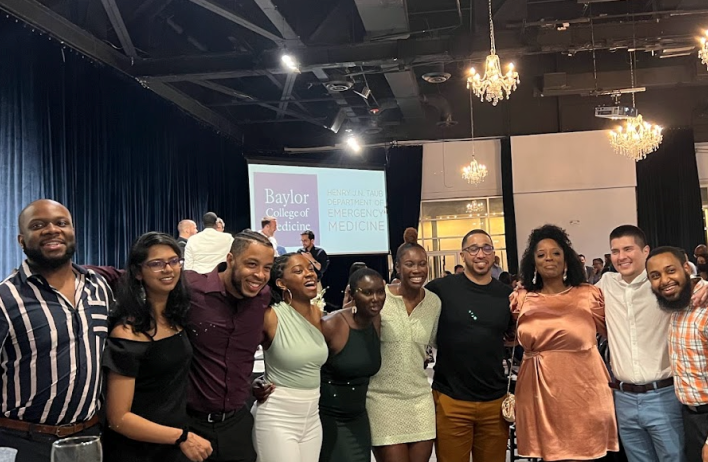 Emergency Medicine Residency Wellness members gather during a group meeting. They stand shoulder-to-shoulder in a long row.