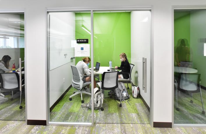 Two students work in a private room with glass doors