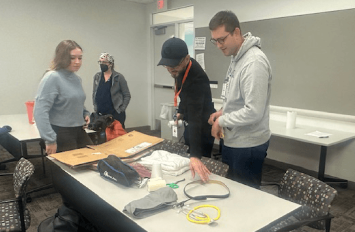 Students look over an assortment of items, including scissors, a cardboard box and a golf bag