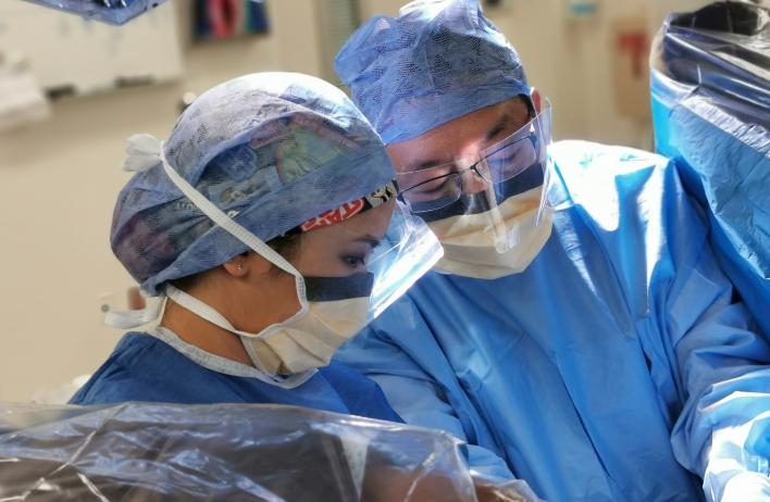 Two people wearing blue surgical scrubs looking over an exam table.