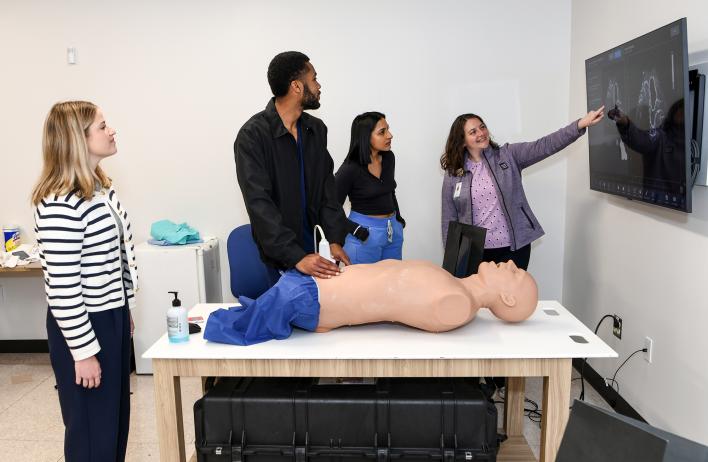 Students standing around a simulation body while looking at a readout screen of their work.