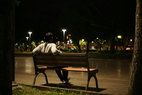 Photo of a man sitting on a bench overlooking a cityscape at night.