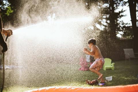 Photo of a child running through the spray of a water hose. 