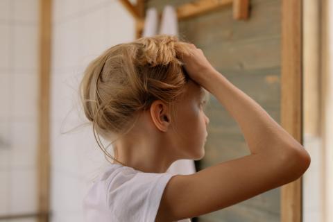 A photo of a girl holding her hair up because her head itches. She has lice! 