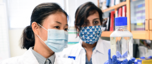Two researchers wearing face masks work in a lab.