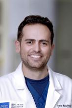 man with short dark hair and a doctor coat smiling