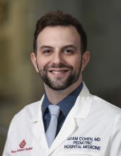 man with white doctor coat and light blue tie smiling