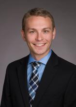 man in dark blazer and light blue shirt smiling