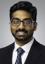 man in a dark suit with glasses smiling