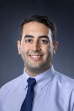 man in blue shirt and navy tie smiling