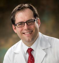 man with dark brown hair and glasses smiling