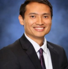 man with black blazer and purple tie smiling