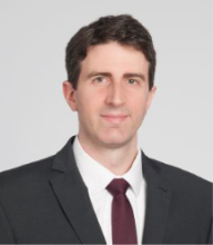 man in grey blazer smiling slightly