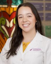 woman with long dark hair smiling in a white doctor coat