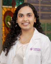 woman with curly dark hair smiling in a white doctor coat