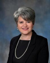 woman in black blazer with a pearl necklace smiling