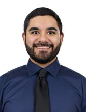 man in deep blue button down and black tie smiling
