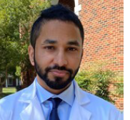 man with dark beard and short hair smiling slightly