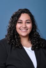 woman with dark curly hair smiling with a black blazer on