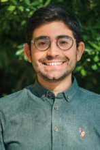 man with short dark hair and round glasses smiling