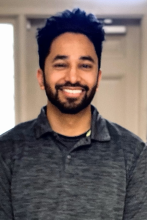 man with dark hair and beard in a grey shirt smiling