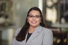 Woman with glass, long dark hair with a light gray blazer and black shirt