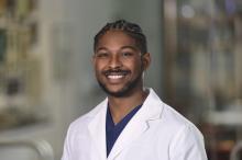 man with braids smiling in a white doctor coat