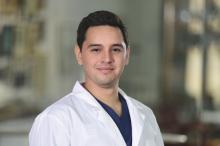 man with dark hair and white doctor coat smiling