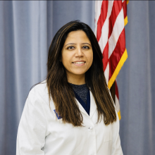 woman with long dark hair smiling in front of flag