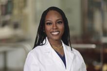 headshot of woman with long braided hair smiling in a white doctor coat