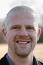 man with buzzcut in a field smiling