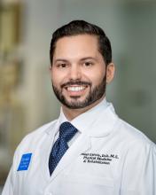 man with short dark hair and a short beard smiling