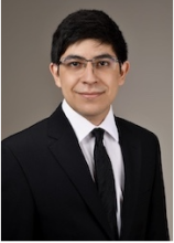 Male with glasses smiling, wearing suit jacket and tie