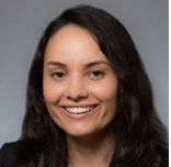Female with long dark hair smiling. Wearing dark suit jacket