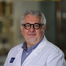 man with glasses and short grey hair in white doctor coat smiling