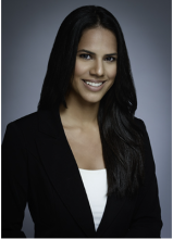 Female with long dark hair, smiling. Wearing dark suit jacket and white undershirt 