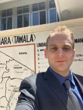 man standing outside with a scientific poster behind him smiling