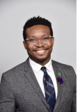Male smiling with gray blazer, black tie, and white button-up shirt