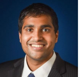 Male with short dark hair, smiling. Wearing dark suit and tie 