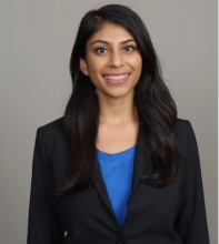 Female with long hair, smiling. Wearing a dark suit jacket and teal undershirt