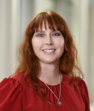 woman with light red hair and a red top on smiling