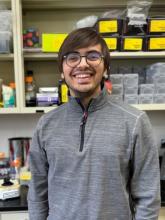 Man smiling in front of a shelf with lab equipment on it