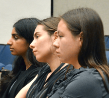 A few people seated in lecture hall chairs watching an offscreen presentation