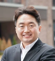 man with short brown hair and a black blazer on smiling