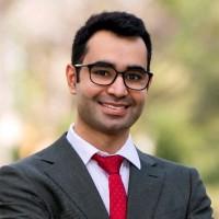 gentleman with dark hair and glasses, wearing gray blazer with red tie