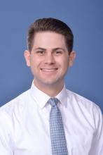 man with a blue tie on and a white button down smiling