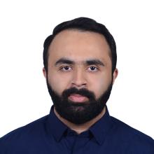Male with short dark hair with dark facial hair, wearing navy blue shirt